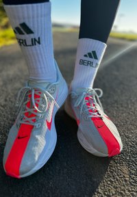 Heledad hallide spordijalatsid erkroosa aktsentidega, hingav võrk ülemine osa ja tekstureeritud tald. Valged soonilised sokid mustade "BERLIN" ja Adidas logo'dega.