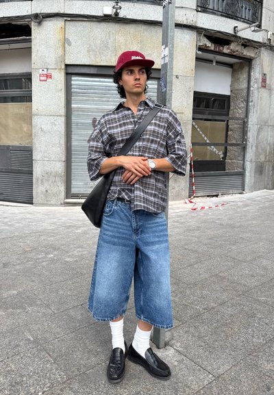 Camisa de cuadros de manga corta, culottes de mezclilla azul de corte holgado, calcetines blancos, mocasines negros y una gorra burdeos con el logo de "Dickies".