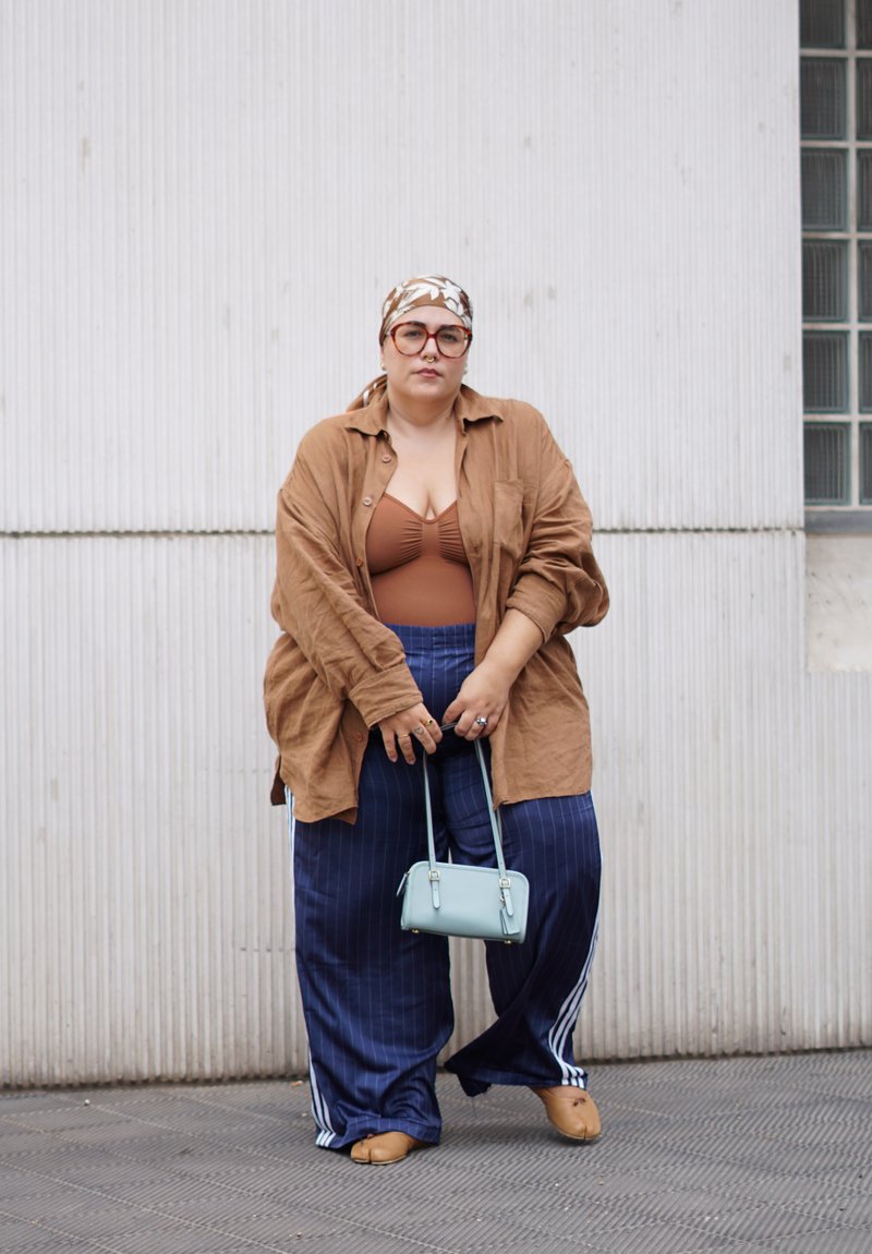 Chemise oversize marron, débardeur marron côtelé, pantalon large à rayures bleu marine, sac à main bleu clair, ballerines marron et foulard à motifs.