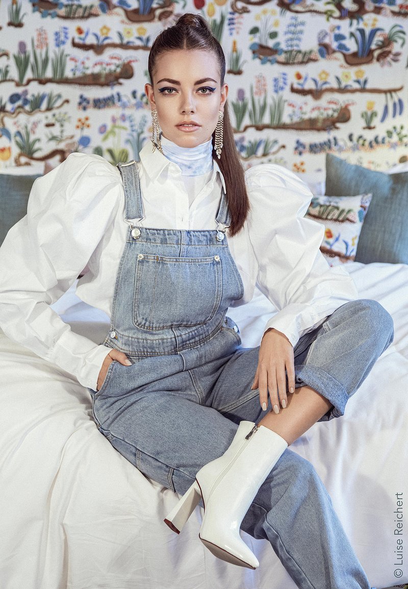 Denim overalls with a relaxed fit, paired with a white puff-sleeve shirt and white glossy ankle boots with a high heel.