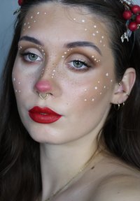 Make-up-Look mit roten Lippen, rosa Nase und weißen Punkten auf den Wangen. Goldener Septum-Ring und Ohrringe ergänzen das Design.