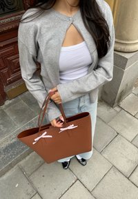 Cardigã cinza de malha com um botão ao nível do decote, top branco por baixo, saia de ganga azul clara e uma bolsa castanha com detalhes em fita rosa.