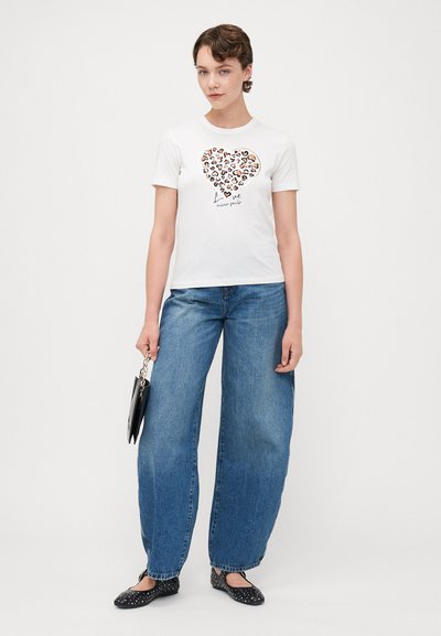 Camiseta blanca de algodón con un diseño de corazón de leopardo, combinada con jeans de mezclilla azul de pierna ancha y zapatos planos negros con tachuelas.