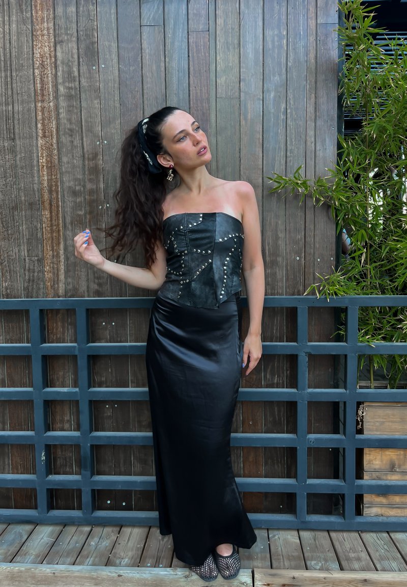 Schwarzes Lederstrapless-Top mit silbernen Nieten, kombiniert mit einem schwarzen Satin-Maxi-Rock. Das strukturierte Top steht im Kontrast zum glatten Rock.