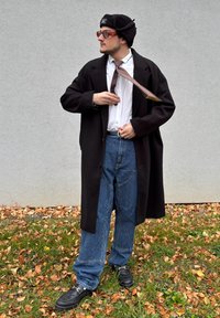 Lång svart kappa, vit skjorta, prickig slips, lösa blå jeans, svarta skor och en svart mössa. Röda solglasögon fulländar looken.