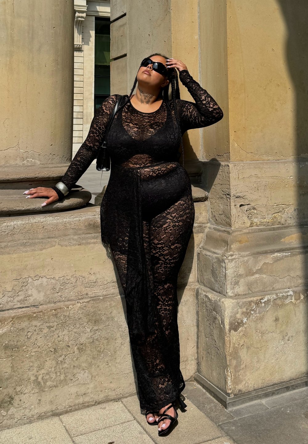 Completo in pizzo nero con maniche lunghe e uno spacco sulla coscia, caratterizzato da un corpetto aderente e un soprabito fluente, abbinato a tacchi neri.