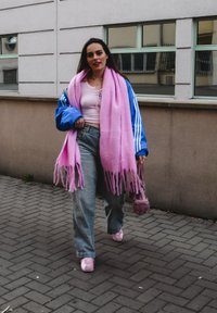 Μπλε τζάκετ Adidas, ροζ υπερμεγέθη κασκόλ, ροζ κοντό τοπ, γκρι τζιν με ψηλή μέση, ροζ αθλητικά παπούτσια και μια μικρή ροζ τσάντα. Φόντο με πλακόστρωτο μονοπάτι.