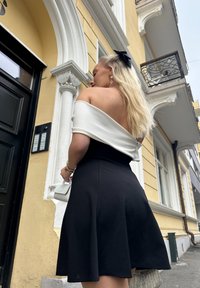 Svart tettsittende kjole med en utswingende skjørt og en avdekket skuldre hvit topp. Inkluderer en liten hvit håndveske og et svart sløyfebånd i håret.
