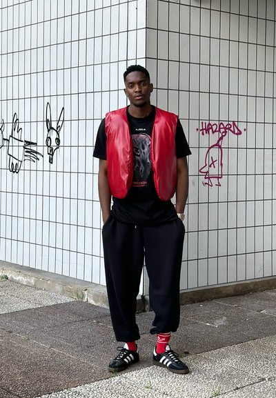 Chaleco de nailon rojo sobre una camiseta negra con gráfica, combinado con pantalones de chándal negros y zapatillas negras con franjas blancas y acentos rojos.