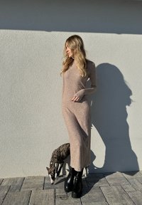 Langes, geripptes Kleid in hellbeige, mit langen Ärmeln und geradem Schnitt. Schwarze klobige Stiefel und ein kleiner Hund darunter.