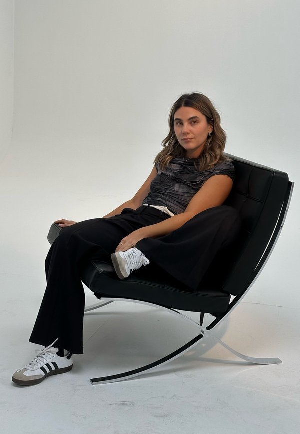 Silla de ruedas de cuero negro con base plateada, con una persona vestida con una camiseta texturizada gris y pantalones anchos negros, usando zapatillas blancas.