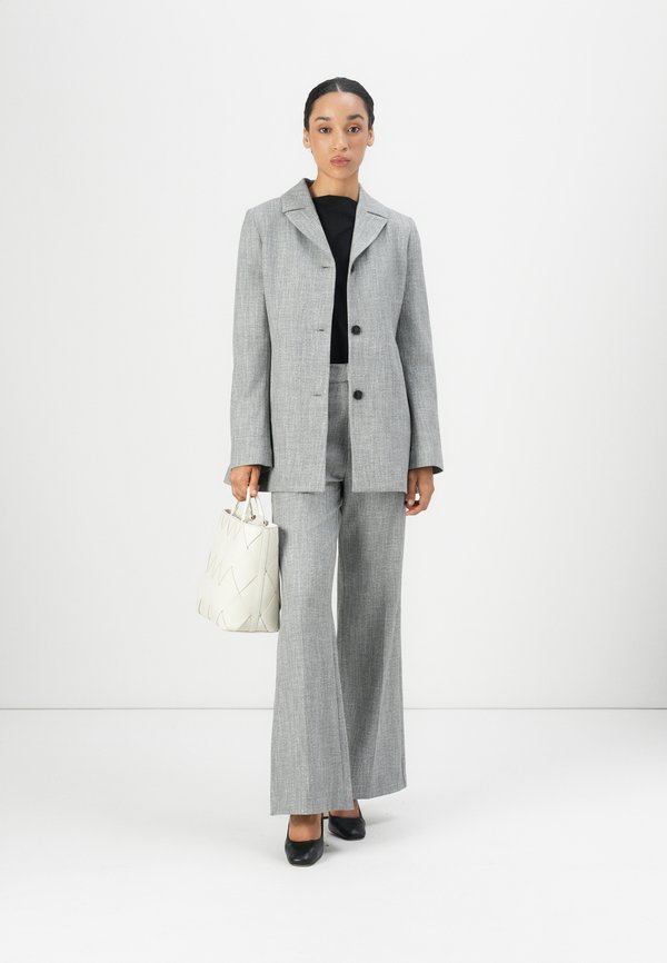A grey tailored suit featuring a long jacket and wide-leg trousers. Worn with a black top underneath, complemented by a cream handbag and black shoes.
