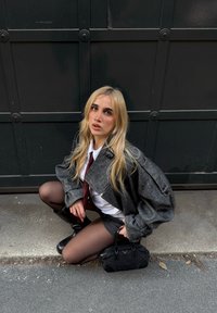 Giacca oversize grigia a spina di pesce, camicia bianca, cravatta rossa e pantaloncini. Collant neri e stivali al ginocchio. Piccola borsa nera come accessorio.