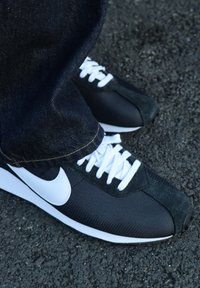Zapatillas deportivas negras y verde oscuro con cordones blancos y un logo blanco. El diseño presenta una tela texturizada y acentos de ante.