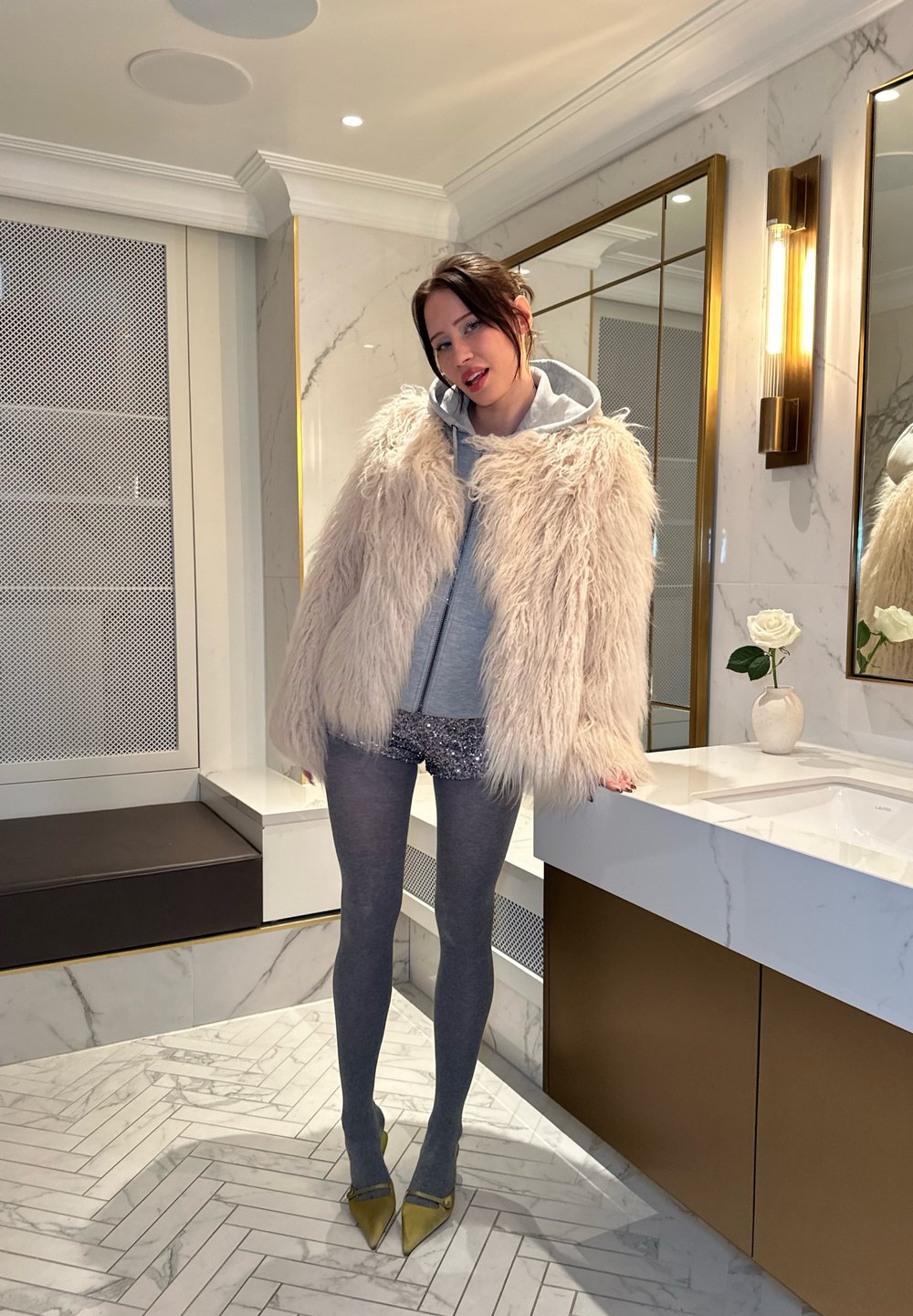 Mākslīgā kažokāda gaiši bēšā krāsā, pelēks kapucis, mirdzošs šorts, pelēkas zeķbikses un dzelteni zābaki. Mūsdienīgs vannas istabas interjers ar marmora un zelta akcentiem.