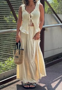 Top in crochet con pizzo, gonna maxi beige, borsa in paglia intrecciata con dettagli neri e sandali piatti con cinturini decorativi.