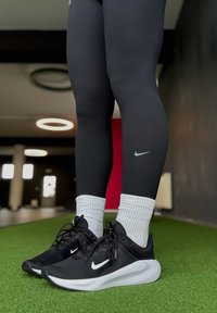Sorte atletikleggings med et lille Nike-logo, kombineret med sorte sneakers med hvid sål og snørebånd, båret med hvide ribstrikkede sokker.