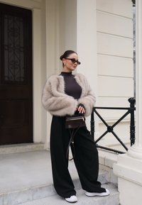 Ψεύτικη γούνα κοντό κάμισο σε ανοιχτό μπεζ, μαύρο εφαρμοστό ζιβάγκο, φαρδιές μαύρες παντελόνες και λευκά παπούτσια. Μικρή μαύρη τσάντα χιαστί με χρυσά αξεσουάρ.