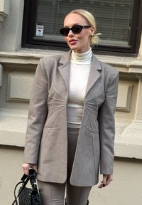 Helehall hall bleiser struktureeritud õmblustega, nööpidega esiküljel ja sälklapiga, kantud valge kõrge kaelusega kampsuni ja ühtivate pükstega. Must mini käekott.