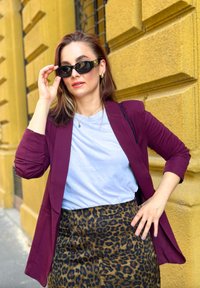 Bordeaux blazer over een lichtblauw T-shirt, gecombineerd met een rok met luipaardprint. Zwarte zonnebril met gouden accenten. Gladde texturen en een aansluitend ontwerp.