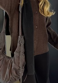 Barna bordázott kardigán gombos záródással, fekete felsővel �és nadrággal párosítva. Egy sötétbarna válltáska határozott textúrával és fém díszítéssel.