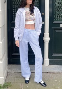 Γκρι φούτερ με φερμουάρ πάνω από ένα κομμένο λευκό μπλουζάκι με γραφικά. Ανοιχτό μπλε ριγέ παντελόνι με φαρδιά μέρη. Μαύρα παπούτσια με λευκές λεπτομέρειες.