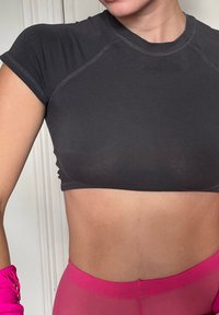 Siv gray crop top s kratkimi rokavi, izdelan iz gladkega materiala. Opoznavne šivane podrobnosti ob ramenih. Usklajen s pink legginsom.