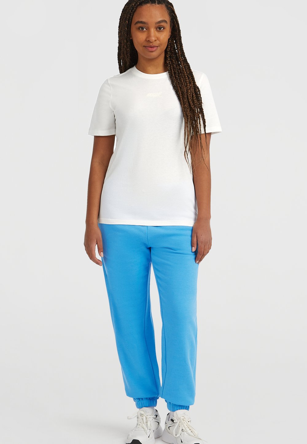 T-shirt bianca a maniche corte con logo, abbinata a pantaloni della tuta azzurri chiari con polsini elasticizzati e sneakers bianche. Un look semplice e casual.