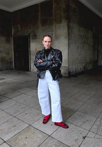 Must musta nahkjope, must ülikond, valged laiad püksid ja punased võrgusandaalid. Väliskeskkond tekstuuriga hallide kiviseintega.