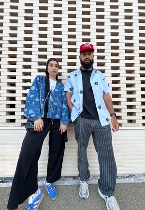 Blue floral-patterned blouse, black wide-leg pants, blue sneakers. Light blue shirt with black flowers, striped pants, and sneakers. Textured wall backdrop.