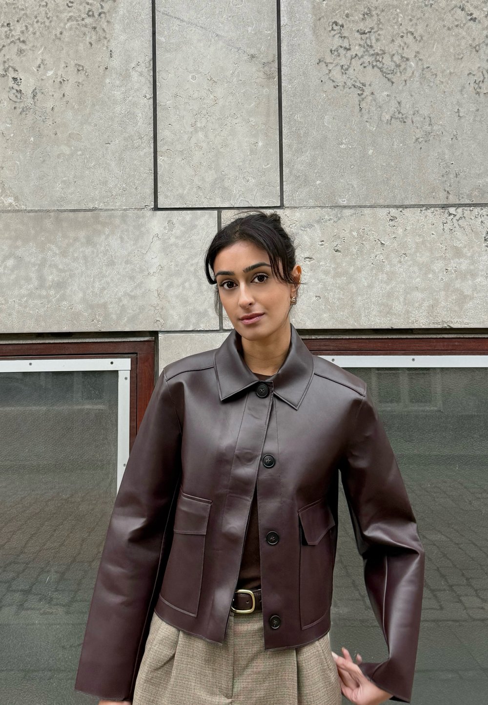 Braune, kurze Lederjacke mit Kragen, Knopfleiste und zwei Vordertaschen, kombiniert mit beigen, karierten Hosen.