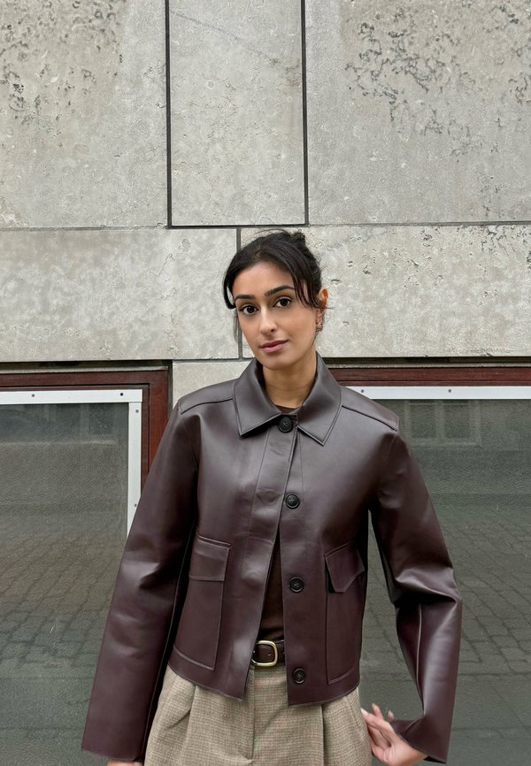 Brun cropped læderjakke med krave, front med knapper og to forlommer, kombineret med beige ternede bukser.