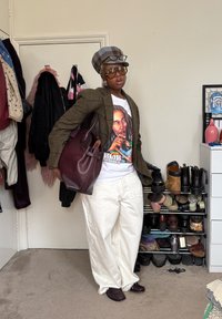 Άτομο που φοράει υπερμεγέθη λευκά παντελόνια, μπλουζάκι Bob Marley, καρό σακάκι και καπέλο, μεγάλα γυαλιά ηλίου και κρατάει σκούρο καφέ τσάντα μέσα σε εσωτερικό χώρο.