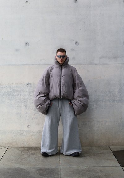 Chaqueta gris esponjosa con mangas oversized, cuello alto y cremallera frontal, combinada con pantalones de chándal gris holgados y zapatos oscuros.