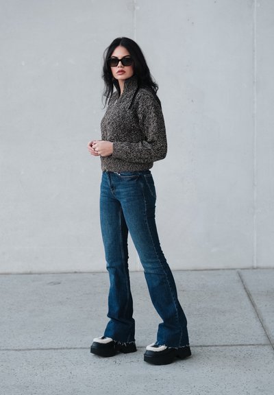 Suéter de punto en marrón y negro, diseño de cuello alto; combinado con vaqueros acampanados azules. Zapatos plataforma negros con detalles de borrego.