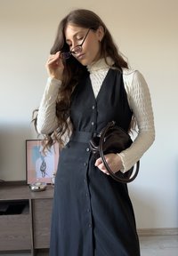 Rochie neagră fără mâneci cu nasturi în față, combinată cu un helancă alb texturat. Accesorizată cu o geantă mică, maro închis.