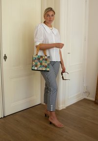 Camisa blanca con cuello, pantalones de cuadros en blanco y negro, sandalias de tiras color marrón y un bolso de patchwork con asa trenzada.