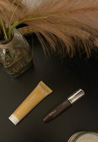 Gul tub av ISADORA CC-kräm med silverlock, märkt "Fuktgivande & SPF 30," bredvid en mörkbrun KIKO-mascara med silverdetaljer.