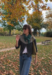 Cardigan lavorato a maglia con un motivo geometrico in crema e grigio, abbinato a una sciarpa verde. Indossato con jeans blu e portando una borsa verde.