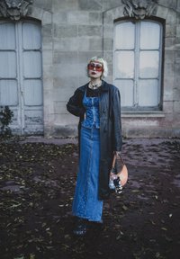 Jeansoutfit med korsettopp och lång kjol, lager-på-lager med en svart läderrock. Accessoarer inkluderar orange handväska och stora röda solglasögon.