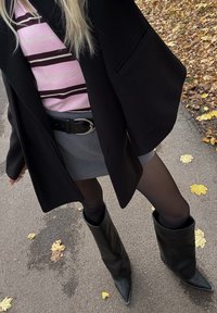 Črni plašč preko roza in rjave črtaste majice, siva krilo, črne nogavice in črni usnjeni škornji do kolen s koničastim prstom. Jesensko listje na tlakovanem površju.