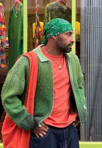 Πράσινη φουντωτή ζακέτα επάνω από ένα κόκκινο μπλουζάκι, σε συνδυασμό με σκούρα τζιν. Μια πράσινη μπαντάνα και χρυσά κοσμήματα ολοκληρώνουν την εμφάνιση.