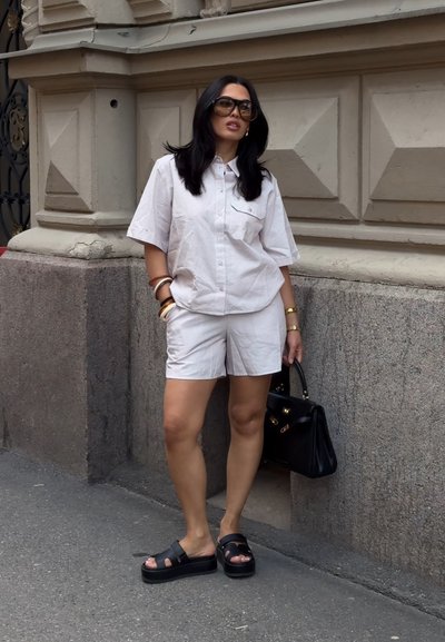 Camisa de botones de manga corta con rayas estrechas, combinada con pantalones cortos a rayas. Sandalias de plataforma negras y un bolso negro completan el conjunto.