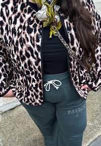 Leopardenmuster gesteppte Jacke mit schwarzem Besatz, kombiniert mit dunkelgrünen Jogginghosen mit weißem Kordelzug und einem schwarzen Oberteil.