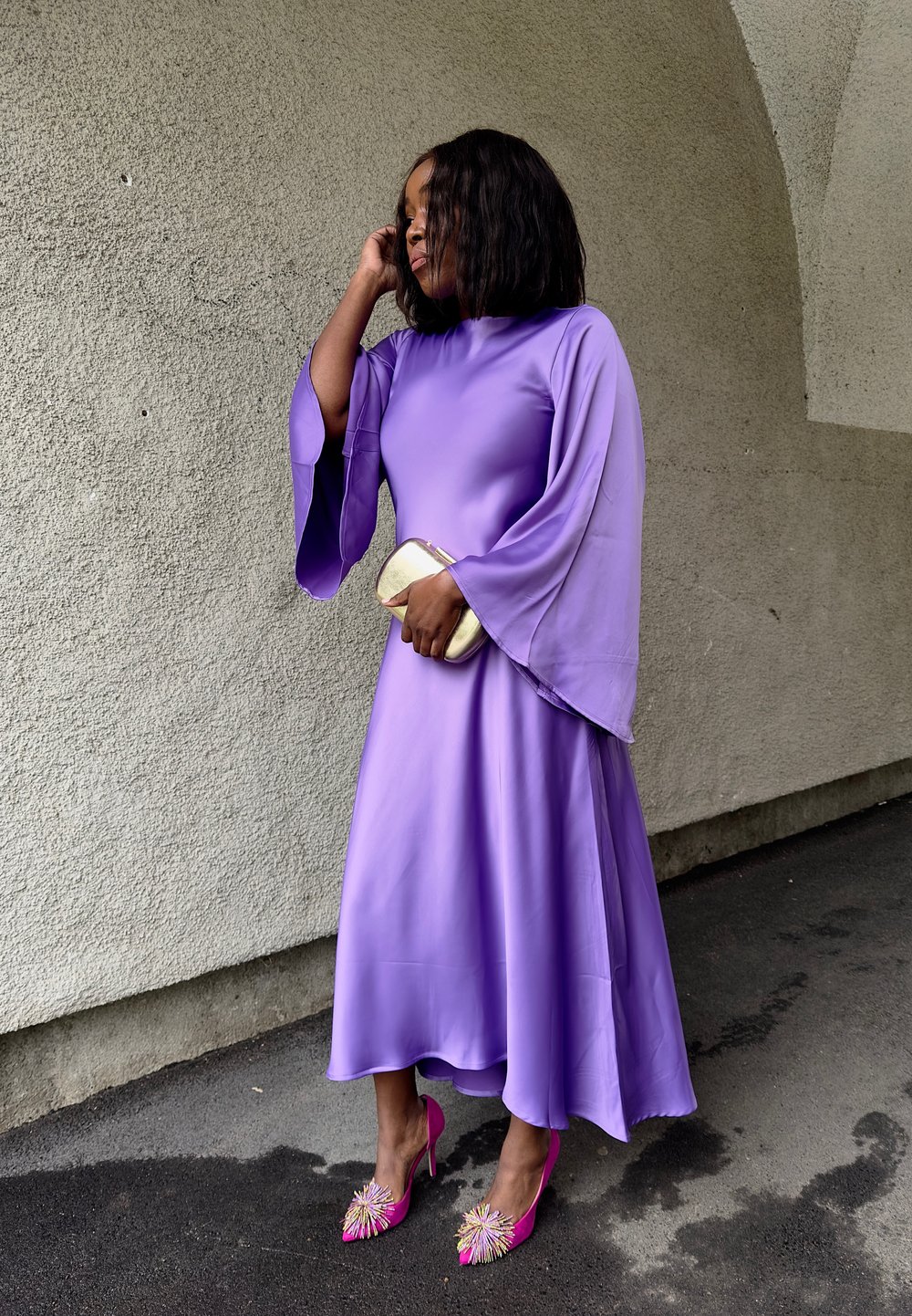 Abito di raso viola con maniche a campana e una gonna fluente. Abbinato a tacchi a stiletto rosa decorati con elementi ornamentali.