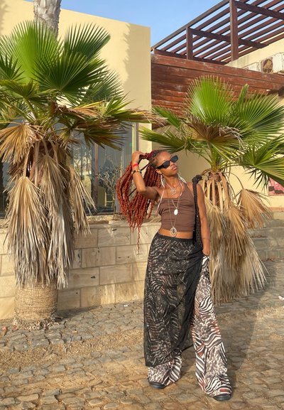 Top marrón ajustado combinado con una falda maxi negra transparente con un patrón de cebra, adornado con collares en capas y gafas de sol.