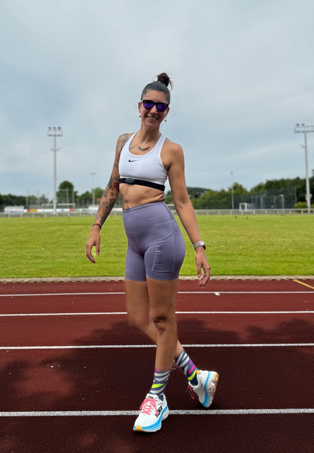 Athlete in a white sports bra and lavender high-waisted shorts, wearing colorful striped socks and light blue running shoes on a track.