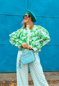 Takkat vihreä ja sininen kukkakuviolla varustettu takki, valkoinen poolopaita, ruutukuosiset siniset housut ja pieni vaalea sininen laukku, jossa on tupsuyksityiskohta.