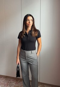 Czarna koszulka polo z krótkim rękawem w połączeniu z dopasowanymi szarymi spodniami. Stylizacja dopełnia czarna torebka i ma gładką fakturę.