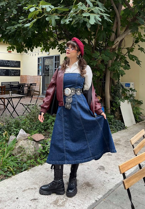 Denim-mekko, jossa on tiukka vartalo-osa ja levenevä hame, yhdistettynä viininpunaisen väriseen bomber-takkiin. Mustat maiharit ja punainen baretti täydentävät asukokonaisuuden.